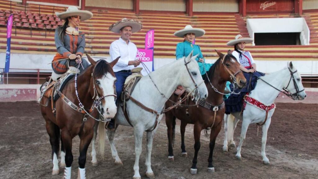 Eduardo Rivera montado a caballo acompaña a charras durante presentación de campeonato de charrería.
