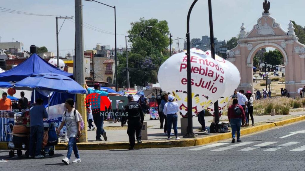 Público que espera ver el desfile del 5 de Mayo muestran globos promocionando a Julio Huerta en la calle.