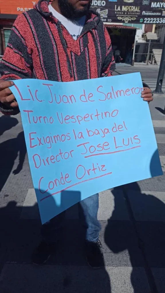 Padre de familia muestra cartel en protesta contra director de primaria, con la leyenda "Lic. Juan de Salmero turno vespertino. Exigimos la baja del director Jose Luis Conde Ortiz".