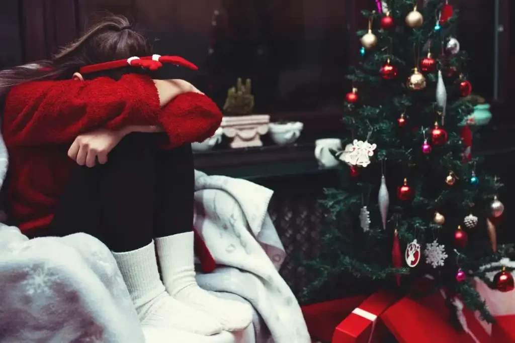 Mujer sentada en un sillón se cubre el rostro y al fondo un árbol navideño.