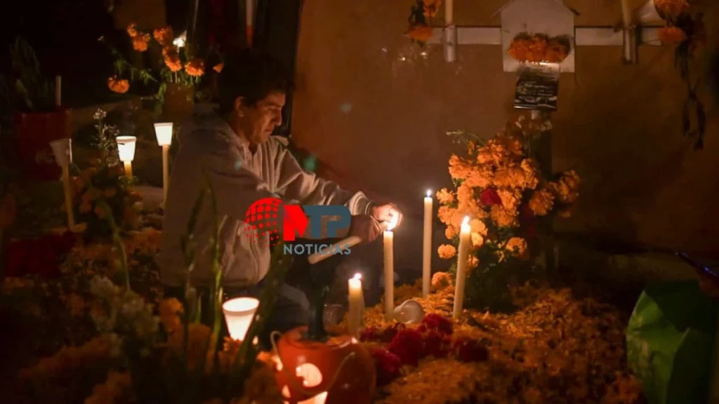 Hombre enciende unas velas que alumbran una lápida, donde yacen sus seres queridos en panteón de La Mixteca.