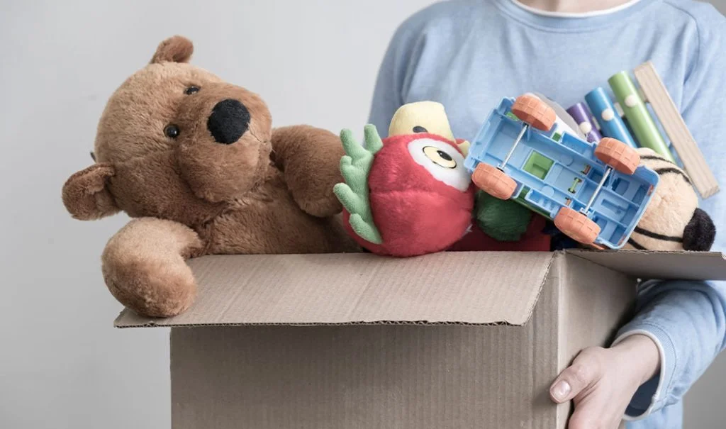 Persona cargando juguetes en una caja d cartón.
