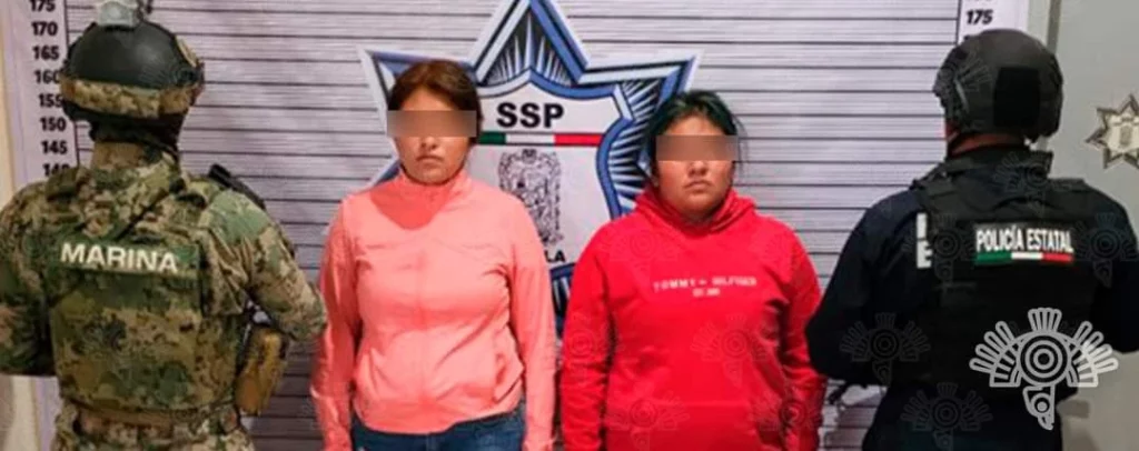 Policía estatal y elemento de la Marina custodian a do mujeres detenidas por robo en Puebla.