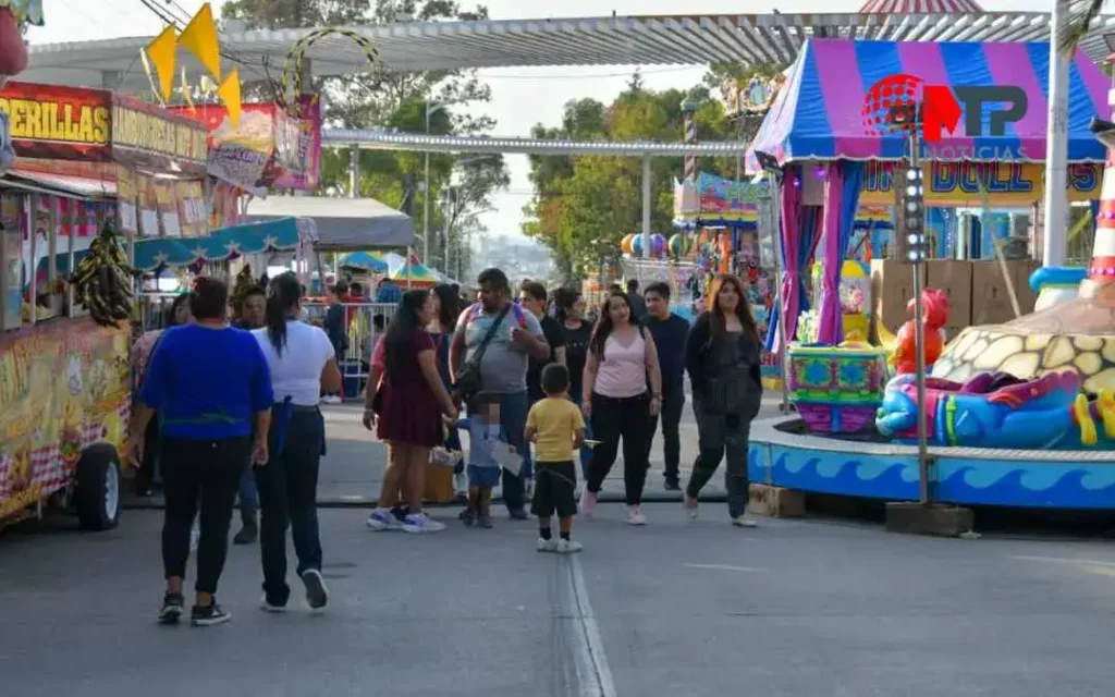 Personas caminan entre los juegos mecánicos de la Feria de Puebla 2024