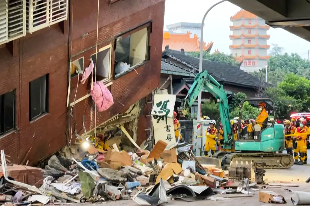 Hombre trabaja con maquinaria al pie de edificio a punto de derrumbarse tras sismo en Taiwán.