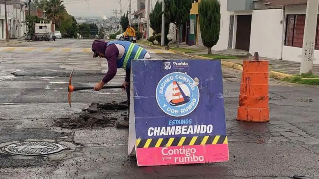 Hombre rasca bache en calle de ciudad de Puebla para repararlo.