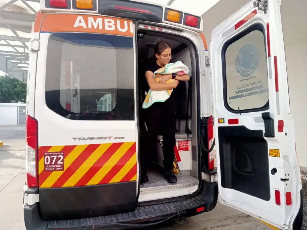Mujer cargando a bebé recién nacido en puerta de ambulancia.