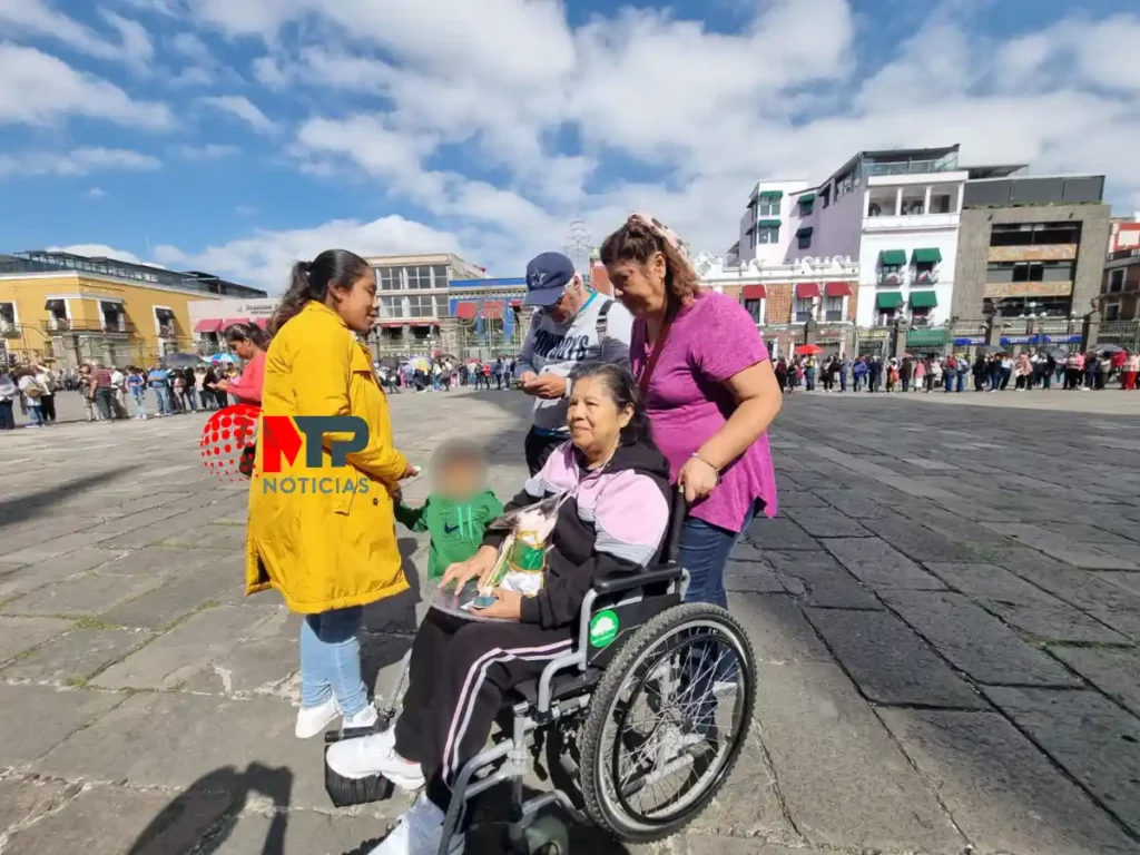 Irene, maestra jubilada en silla de ruedas, regala estampas de San Judas Tadeo afuera de la Catedral de Puebla.